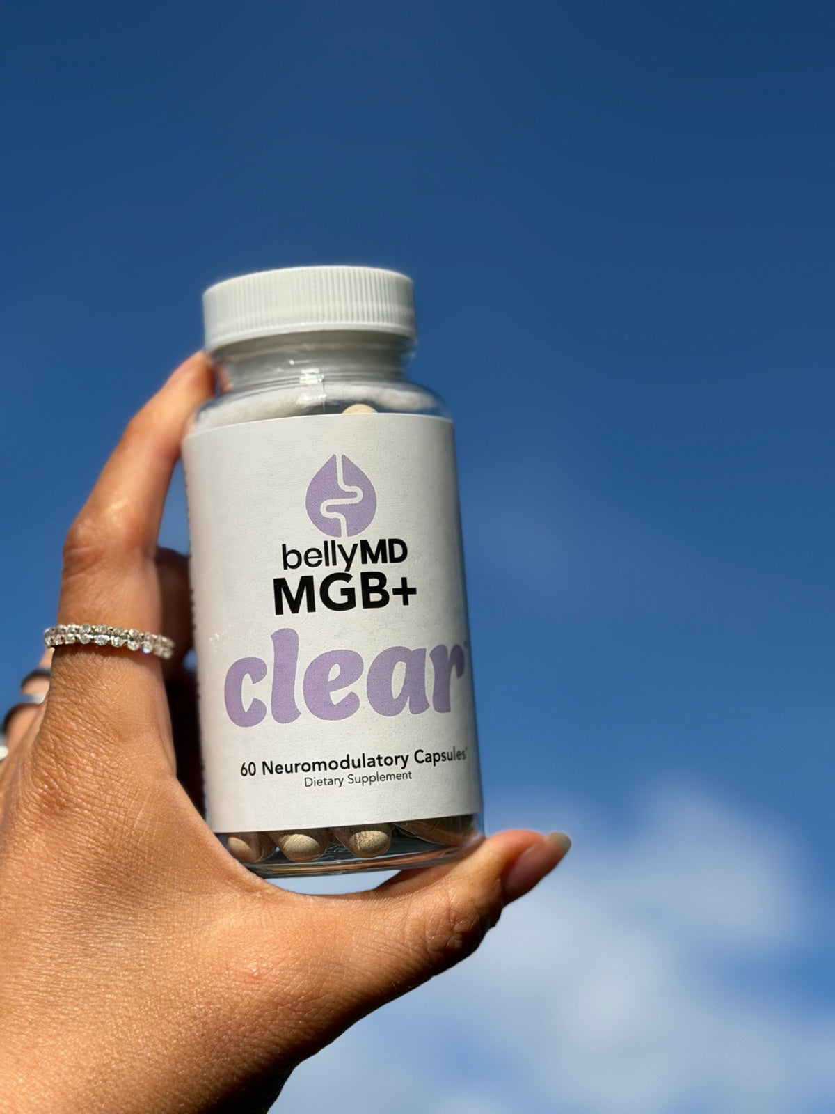 A hand holding a bottle of MGB+ Clear against a bright blue sky